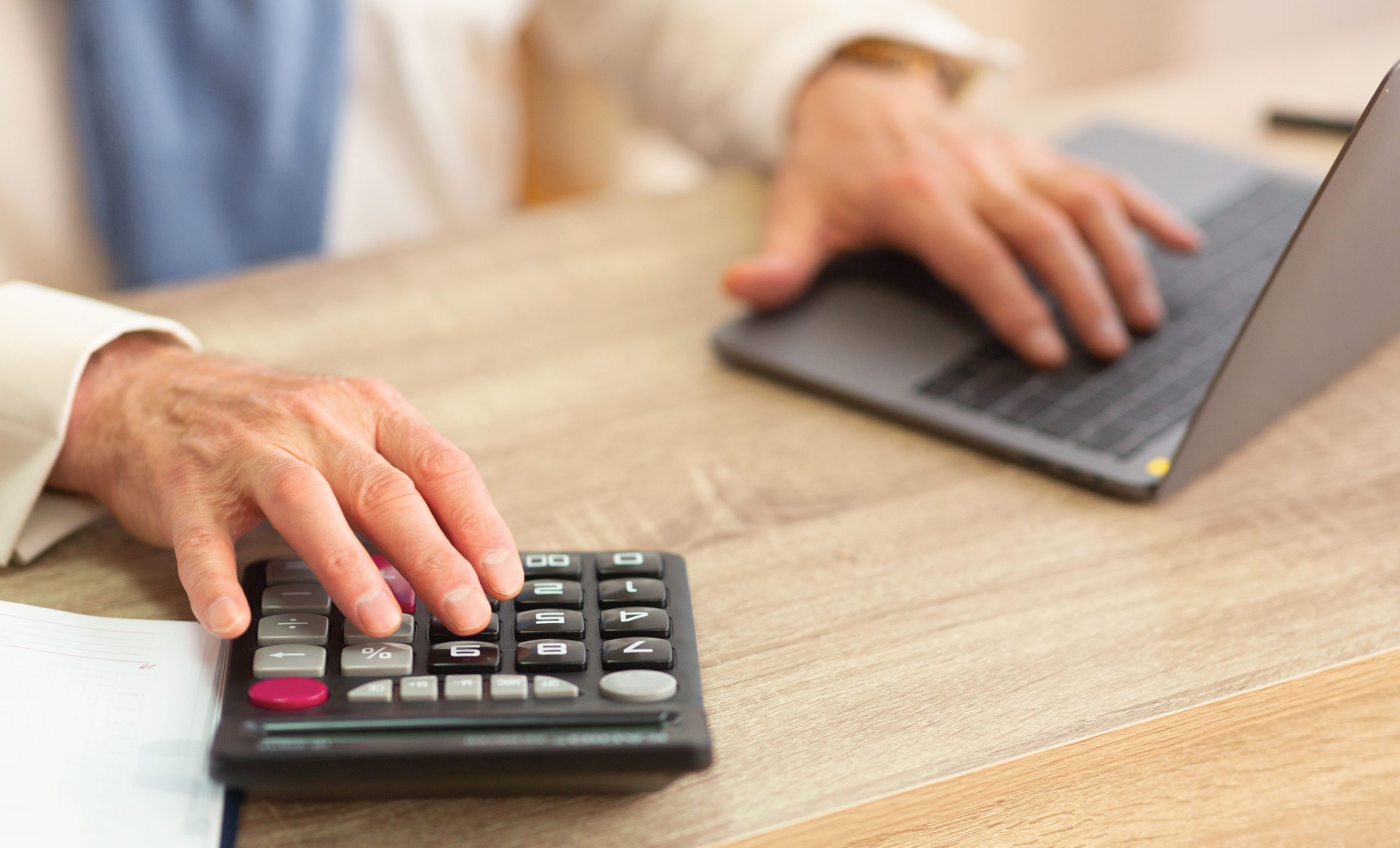 Closeup Of Elderly Man's Hands Calculating Finances Using Calculator And Laptop Sitting In Office. Cropped